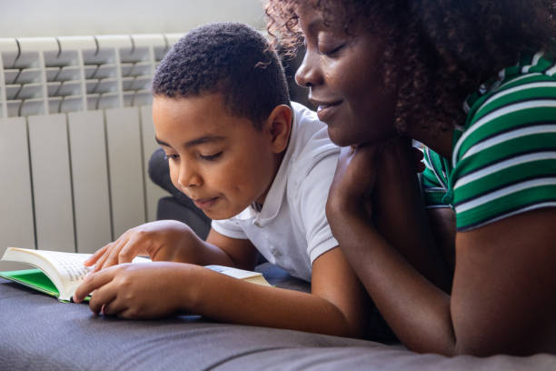 Top view of a mother and son lying on a mat reading a book at home
