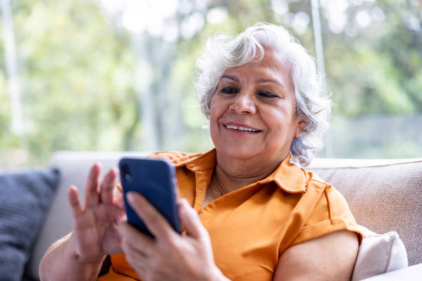 Senior woman texting on her cell phone and smiling Happy Latin American senior woman texting on her cell phone and smiling at home - lifestyle concepts old-phone stock pictures, royalty-free photos & images