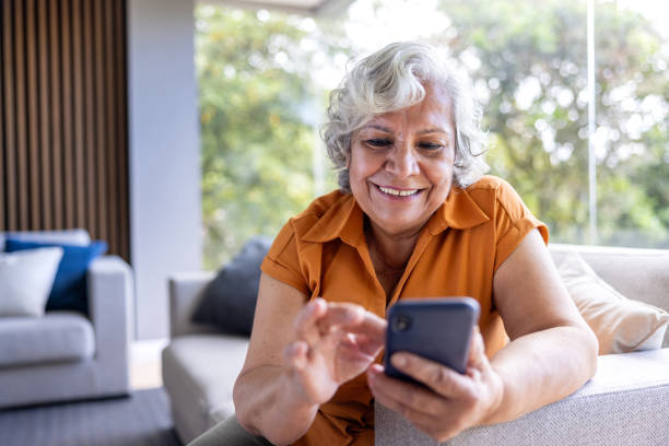 istock Senior woman smiling while using her cell phone at home 2202195033