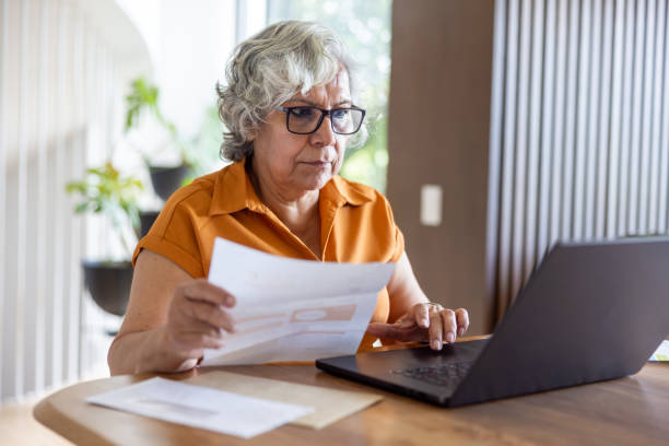 Senior woman at home paying bills online using her laptop