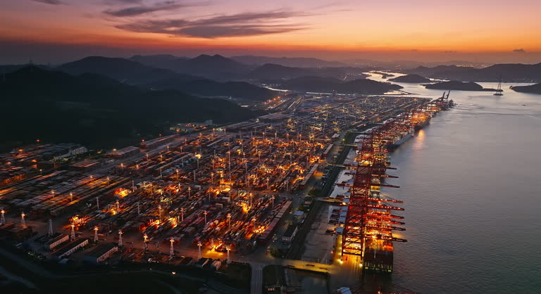 Aerial view of a busy container port at sunset with vibrant lights