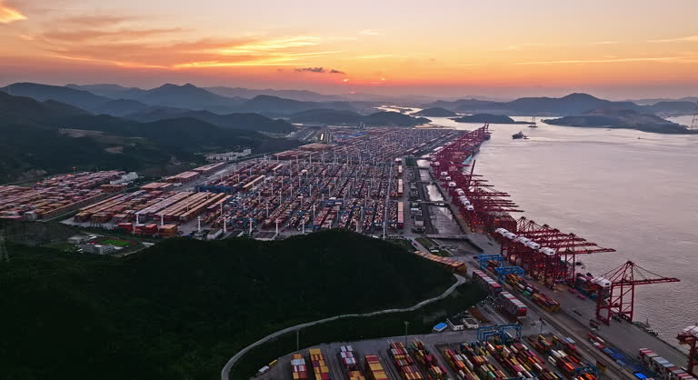 Aerial view of a busy container port at sunset with mountain background