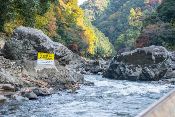 istock Scenic river with warning sign and autumn foliage. at Hozugawa River 2202200744