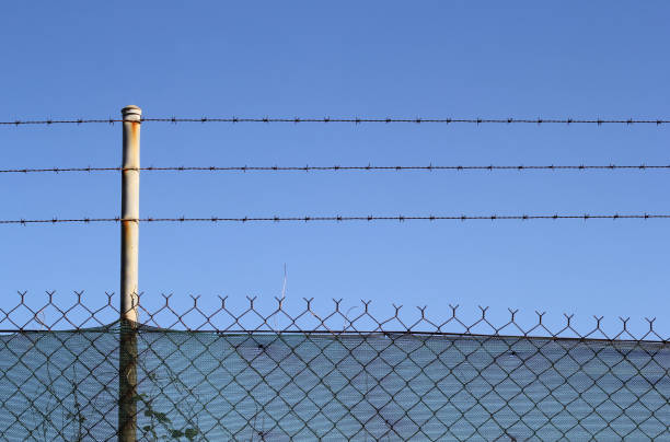 istock Chain link and barbed wire fence against a clear bright blue sky 2202202655