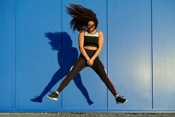 istock Young sporty woman jumping with blue wall background 2202209908