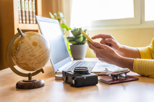 istock Traveler using a smartphone and laptop for booking and planning an exciting trip, surrounded by a globe, camera, airplane model, and passport on a desk 2202211900
