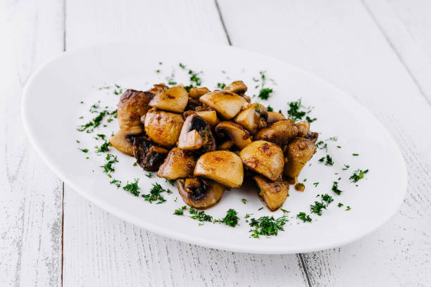 istock Fried mushrooms with dill lying on white plate on white table 2202212115