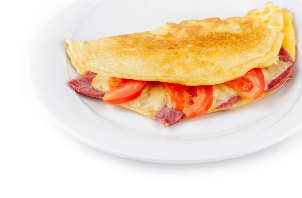 Delicious folded omelette filled with cheese, ham and tomatoes, served on a white plate, isolated on a white background