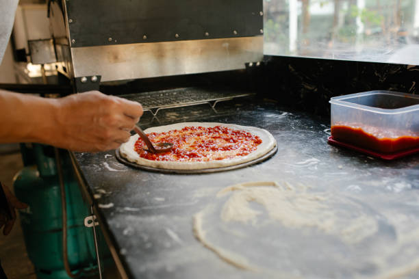 istock Man Spreading Marinara Sauce Onto Pizza Dough 2202217131