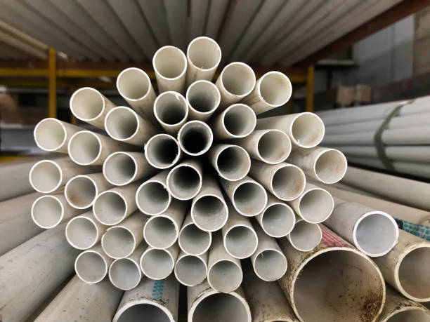istock A neatly stacked bundle of white PVC pipes is arranged in a circular pattern, creating a symmetrical and repetitive geometric design. The pipes are stored in a warehouse with additional piping visible in the background. 2202220846
