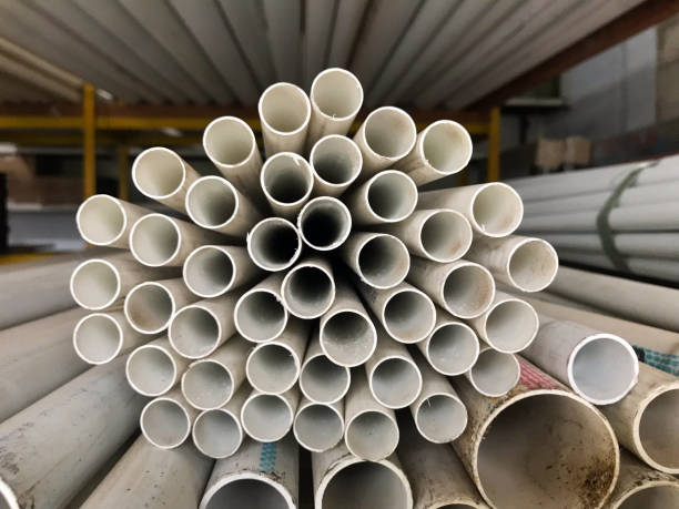 istock A neatly stacked bundle of white PVC pipes is arranged in a circular pattern, creating a symmetrical and repetitive geometric design. The pipes are stored in a warehouse with additional piping visible in the background. 2202220909