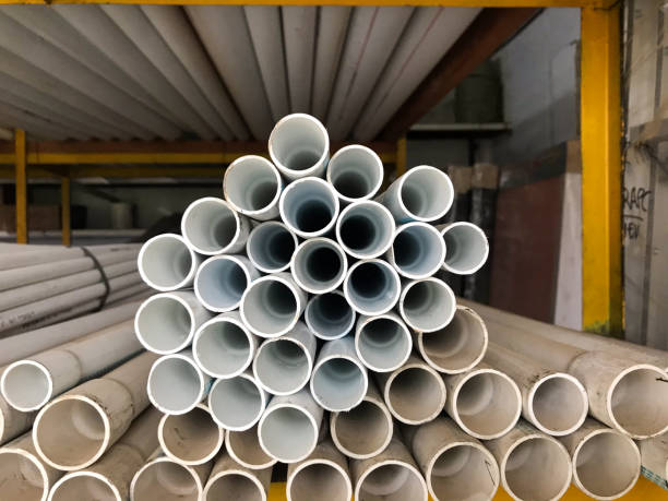 istock A stack of white PVC pipes is arranged in a circular pattern in a warehouse. The pipes vary in size, creating a symmetrical and organized structure. Yellow metal racks and additional pipes are visible in the background. 2202220928