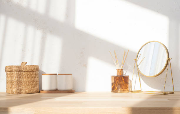 istock Dressing table top with round mirror, aroma sticks and containers on blurred abstract texture wall background in soft window sunlight shadows 2202223711