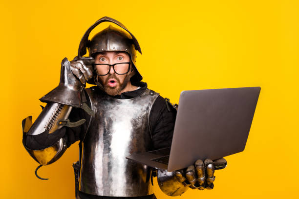 istock Young man in medieval knight armor using a laptop against vibrant yellow background 2202224260