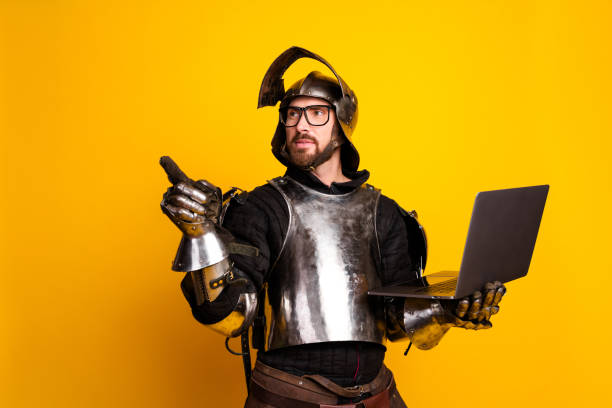 istock Young man wears medieval armor while holding a laptop 2202224263