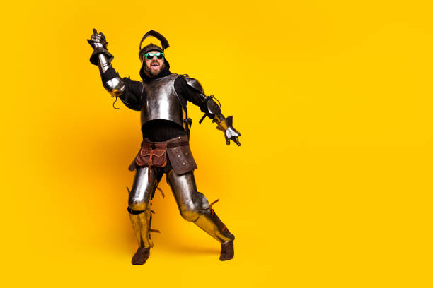 Energetic young man wearing medieval knight armor with modern sunglasses. Set against a bright yellow background. Highlights humor and contrast between historical and modern styles.