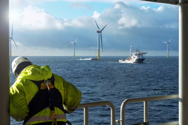 istock Offshore Wind Farm Operations – Worker Observing Service Vessels and wind farm from substation 2202232385