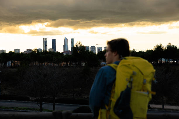 A blurred view of traveler with a yellow backpack looking towards the Madrid's four tower business area as the sun sets