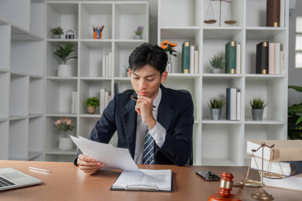 Thoughtful lawyer reviewing legal documents and notes, analyzing case strategy in modern office. A thoughtful lawyer examines legal documents and notes, contemplating case strategy while seated at a desk in a contemporary office environment. civil rights act stock pictures, royalty-free photos & images