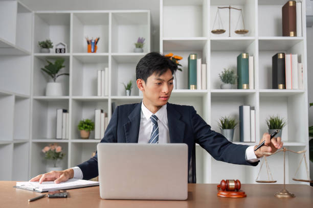 istock Asian lawyer analyzing case files while balancing scales of justice in modern office environment. 2202237461