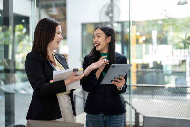 istock Cheerful businesswomen sharing ideas and strategies while holding a tablet and documents in a modern office. 2202238079