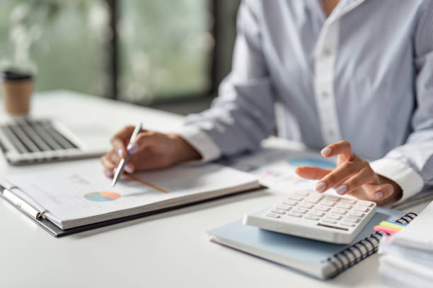 istock Finance worker calculating data with a calculator and reviewing reports in a modern office. 2202241656