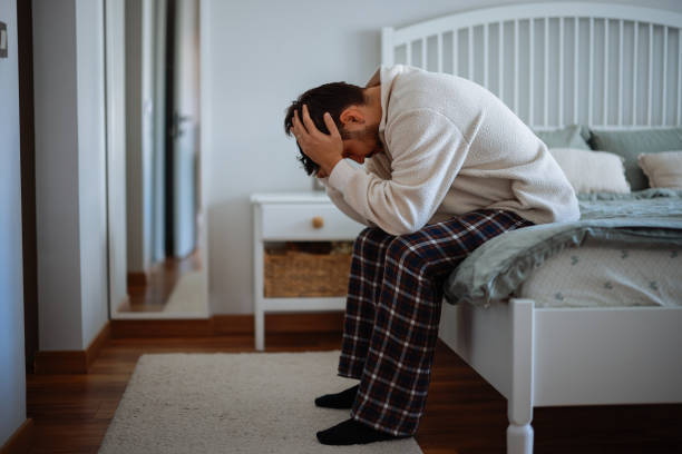 istock Man sitting on bed with head in hands 2202244397