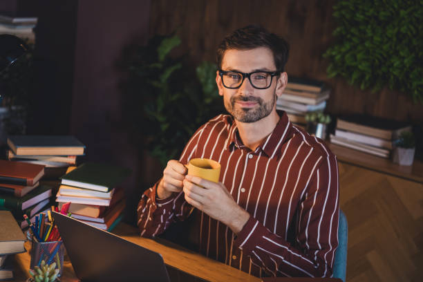 istock Young brunet man enjoying coffee at home while working on a laptop surrounded by books, studying or preparing for late evening work. 2202252189