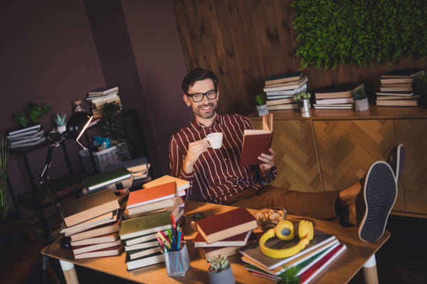 istock Young man reading with a coffee cup in a cozy home interior surrounded by books, creating a relaxed and studious atmosphere 2202252214