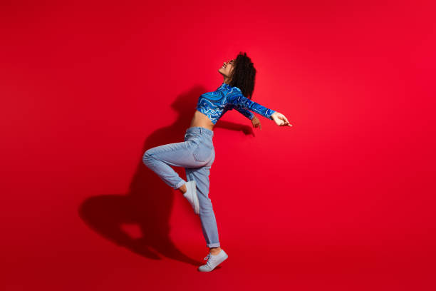 istock Confident young woman posing stylishly on a vibrant red background, wearing a blue patterned top and jeans, showcasing energy and beauty 2202255987
