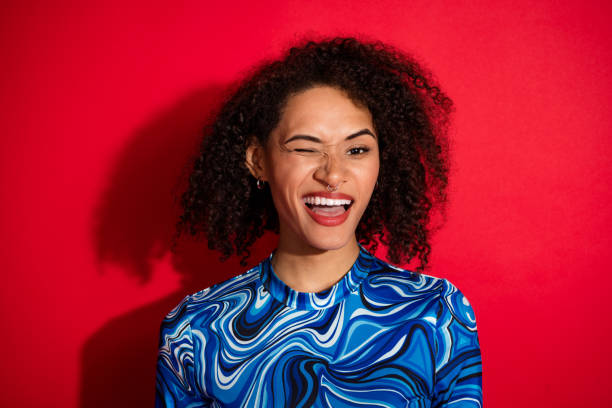 istock Joyful young woman standing against bright red background, wearing trendy patterned top and expressing playful energy 2202256084