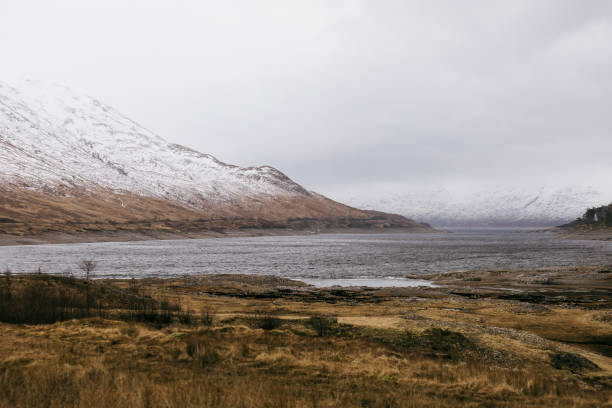 Scenic views of Skye Island showcase rugged mountains covered in snow and tranquil waters reflecting the cloudy sky at dusk.