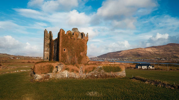 Ruins of a once magnificent castle covered in ivy stand proudly in rural Scotland with hills in the background under a clear sky.