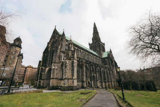 Visitors admire Glasgow Cathedrals impressive gothic architecture while exploring the surrounding grassy area in Scotland.