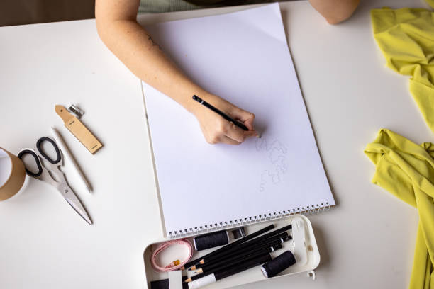 Talented female fashion designer is captured in the midst of her creative process, sketching a new clothing design in her studio.