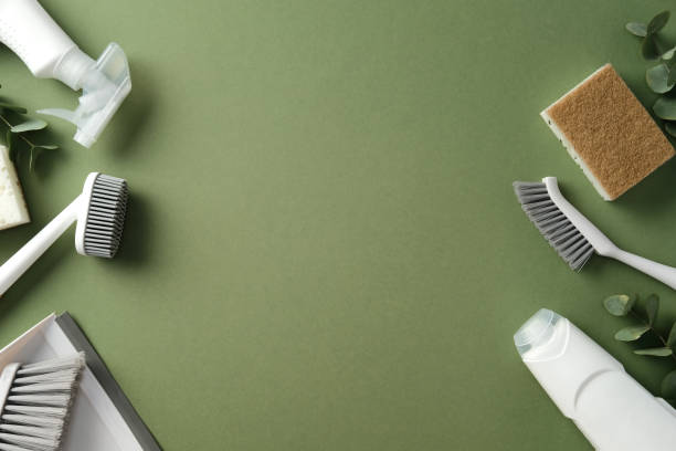 istock Cleaning supplies on a green background. Frame of various tools including brushes, a sponge, and a spray bottle, arranged with leaves for a natural touch 2202260784