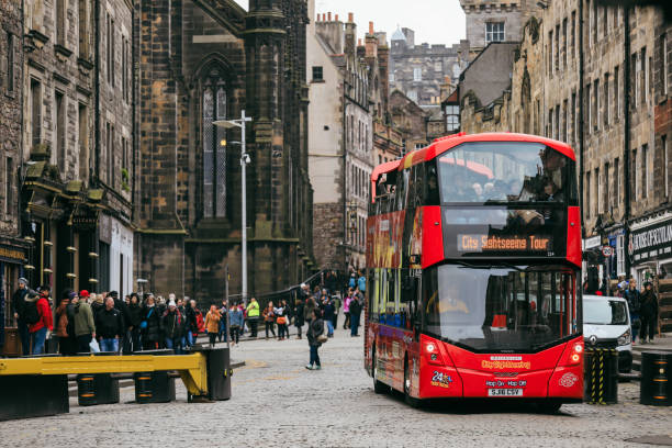 Edinburgh, United Kingdom - November 10, 2024: A red sightseeing bus stops on a cobbled street in Edinburgh, attracting visitors as they enjoy the citys historic charm.