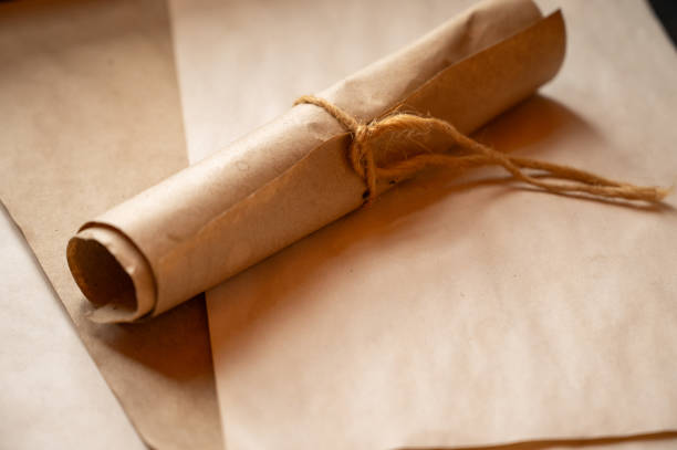 istock A rolled parchment tied with rustic twine, placed on aged paper sheets. The warm tones and natural textures evoke a sense of history, vintage correspondence, or eco-friendly packaging. 2202263073
