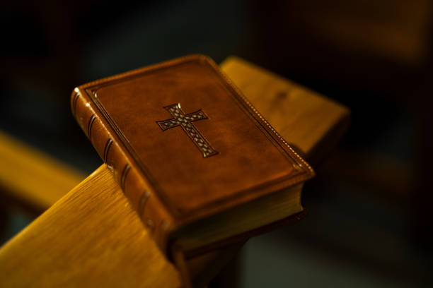A leather-bound Bible with a decorative cross on its cover rests on a wooden church pew, illuminated by warm, soft lighting.
