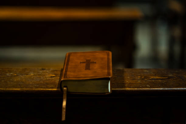 A leather-bound Bible with a decorative cross on its cover rests on a wooden church pew, illuminated by warm, soft lighting.