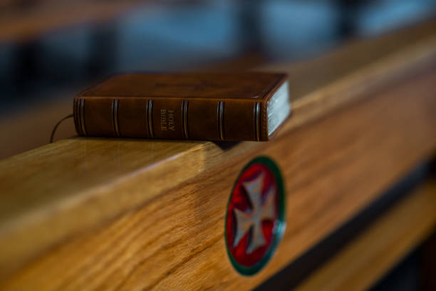 Closed leather-bound Bible featuring a cross on its cover, placed on a rustic wooden table with warm, dramatic lighting.