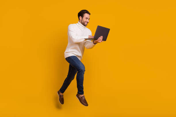 istock Photo of positive pretty guy wear white pullover jumping high writing modern device isolated yellow color background 2202271890