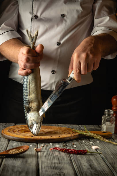 istock A dedicated chef expertly holds a whole fish while preparing it on a wooden cutting board. The kitchen exudes warmth, with spices and herbs adding to the atmosphere of culinary craftsmanship 2202274503