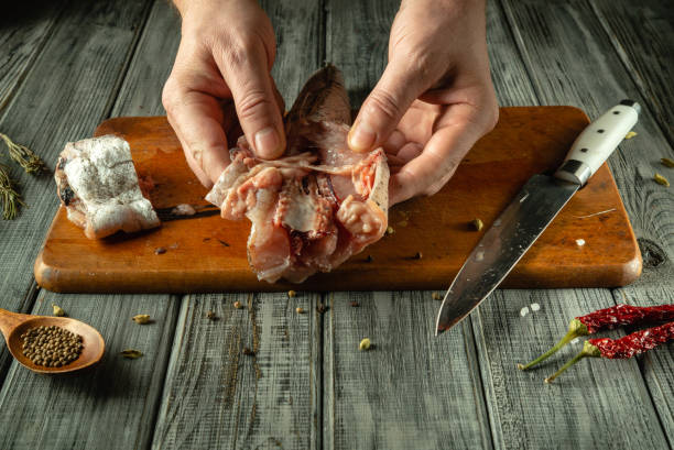 istock Hands expertly handle raw meat fish, showcasing culinary skill in a warm, rustic kitchen. A wooden cutting board, knife, and spices create an inviting atmosphere for cooking enthusiasts 2202274603