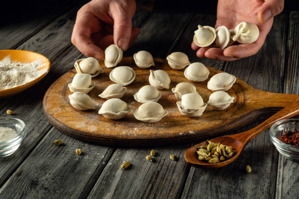 istock Hands are shaping and arranging fresh dumplings on a wooden board. The rustic kitchen features flour, spices, and a warm, inviting atmosphere 2202274980