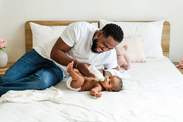 istock Loving African father feeding his baby with a bottle while lying on a cozy bed. A heartwarming moment of fatherhood, bonding, and care, symbolizing modern parenting and nurturing relationships. 2202277145