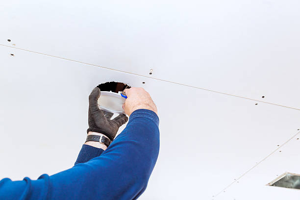 istock Worker installing lighting fixture in drywall ceiling during home renovation project in well-lit room 2202281381