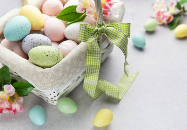 istock Pastel colored easter eggs overflowing from a white wicker basket decorated with spring flowers 2202281527