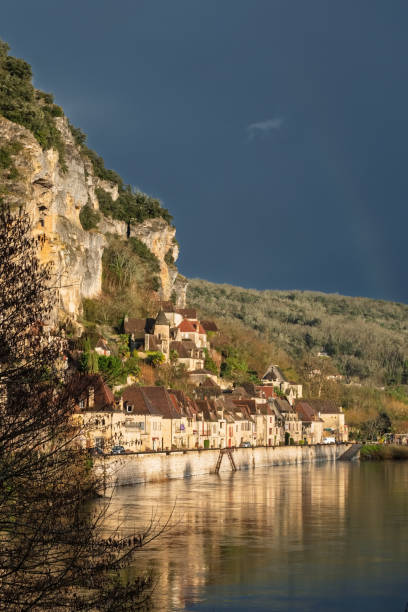 La Roque-Gageac, Dordogne France - 25th February 2025: The village of La Roque-Gageac sitting under darm stormy skies but lit up by evening sun on the Dordogne river in France