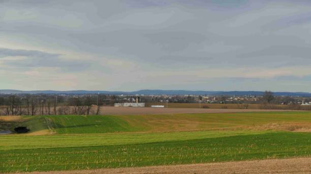 istock Scenic view of rolling green fields contrasting with distant town under a partly cloudy sky 2202288857